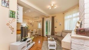 Una sala de estar moderna con televisor, mueble blanco de entretenimiento y sofá. Se ve un comedor con mesa y sillas al fondo.