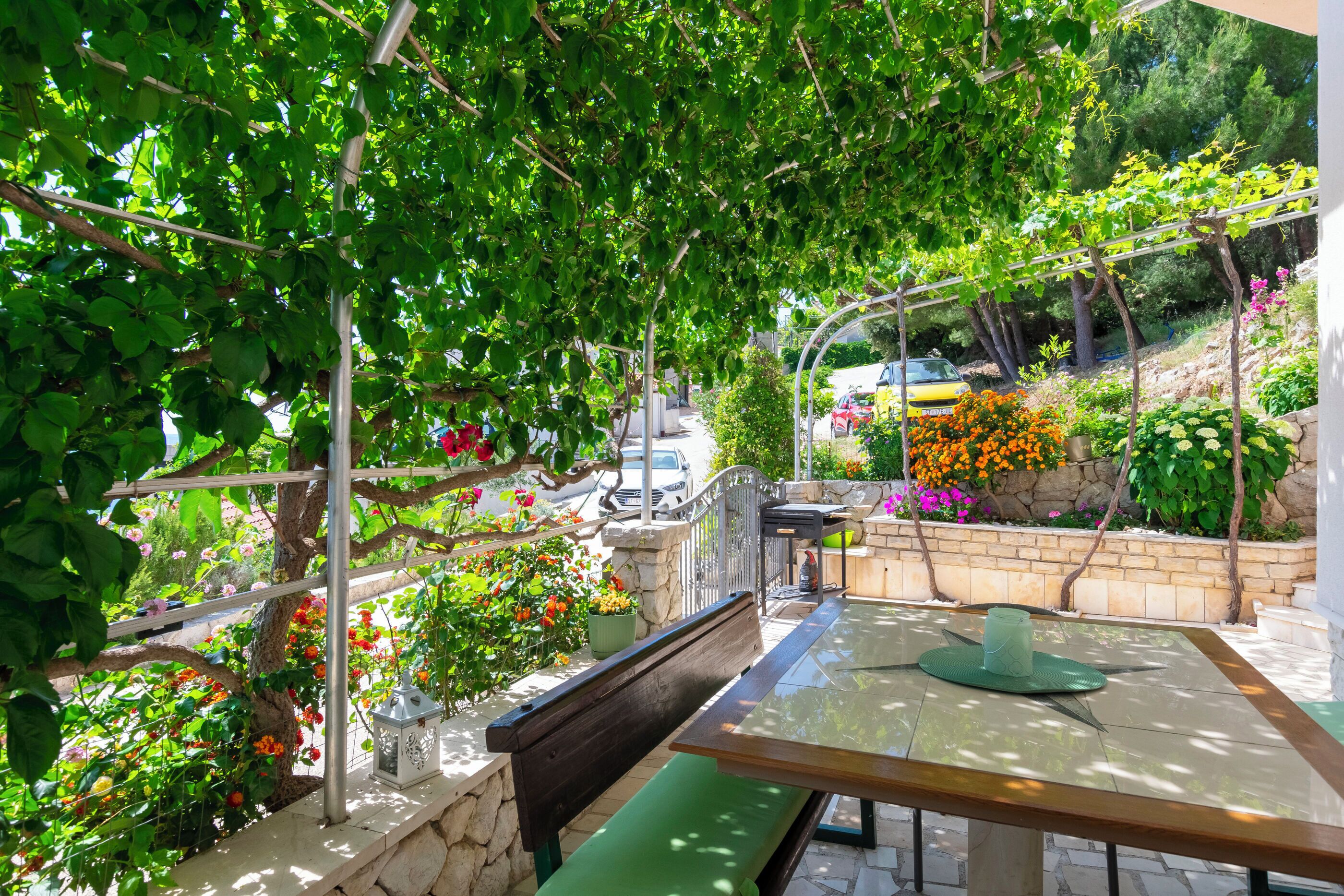 A patio with a table and bench, surrounded by greenery and flowers.