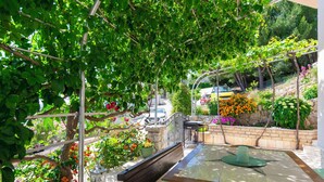 Un patio con mesa y banco, rodeado de follaje y flores.