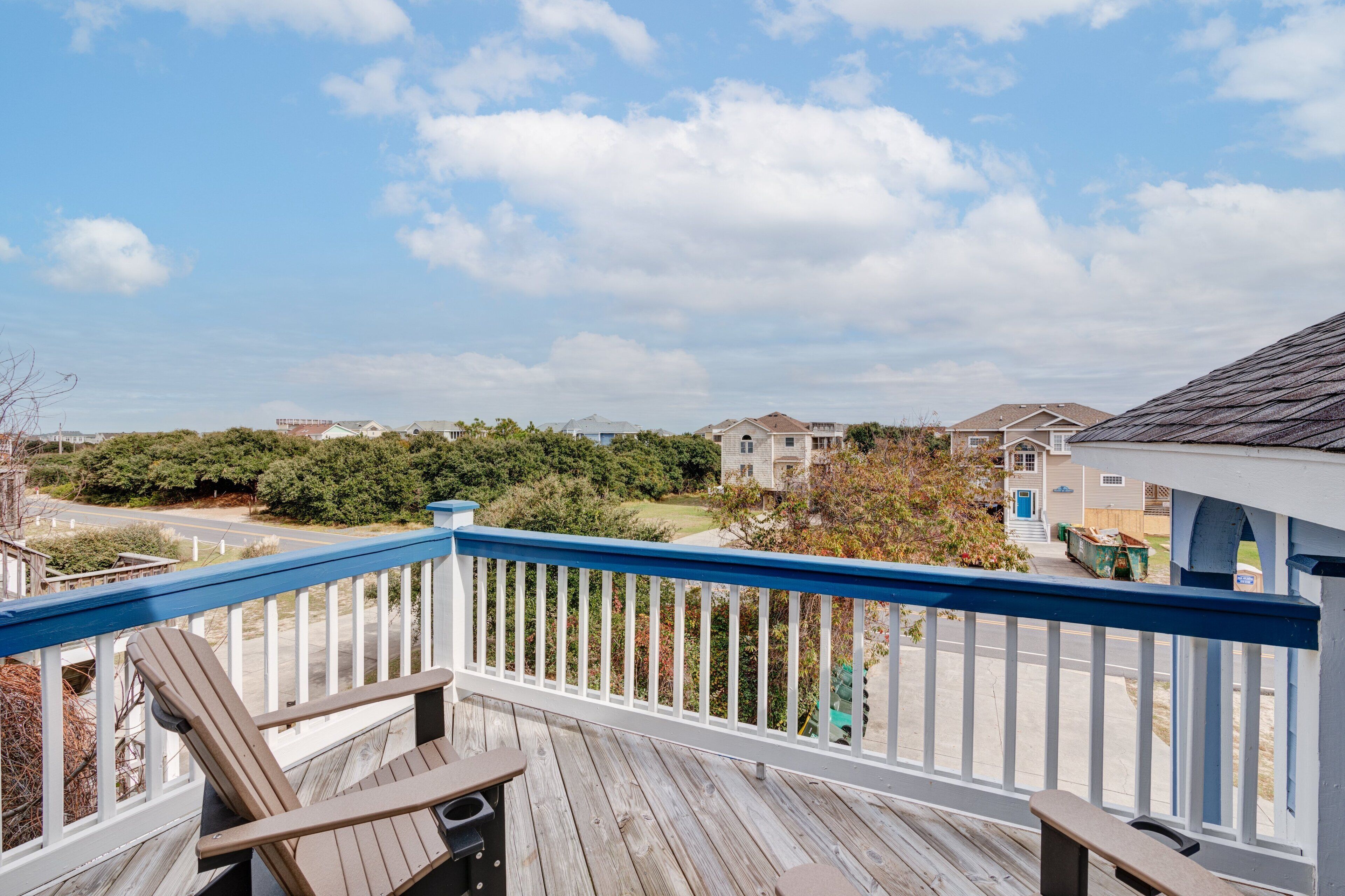 Terraza de madera con barandilla, con vista a una zona residencial con casas y vegetación.