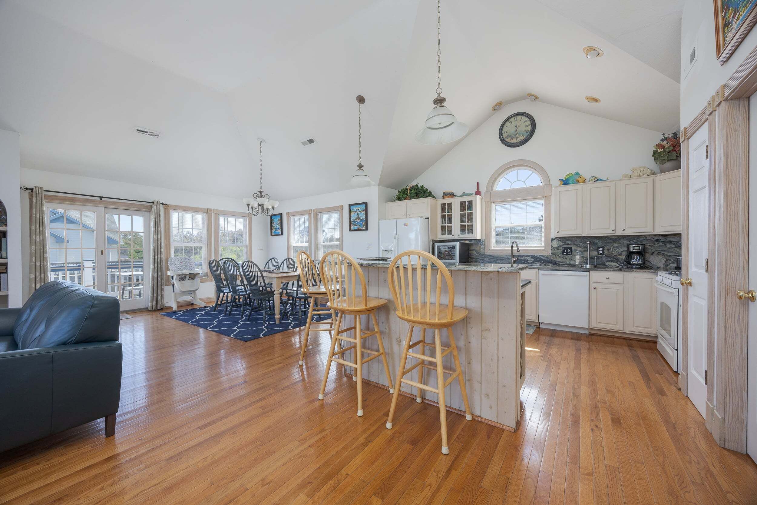 A spacious kitchen with wooden flooring, a dining area with chairs, a sofa, and a large window.