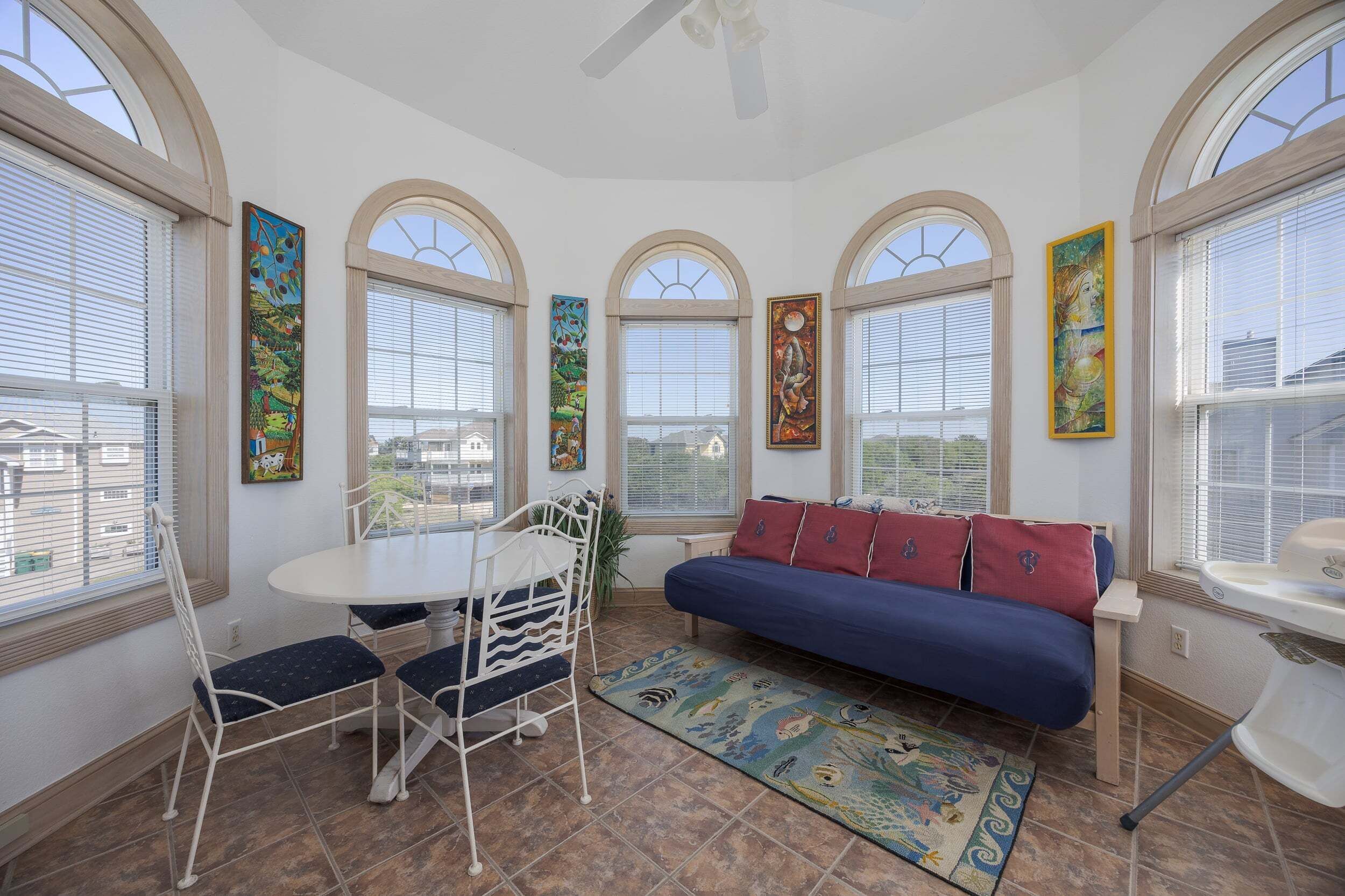 A sunroom with a dining table, chairs, a sofa, and artwork on the walls.