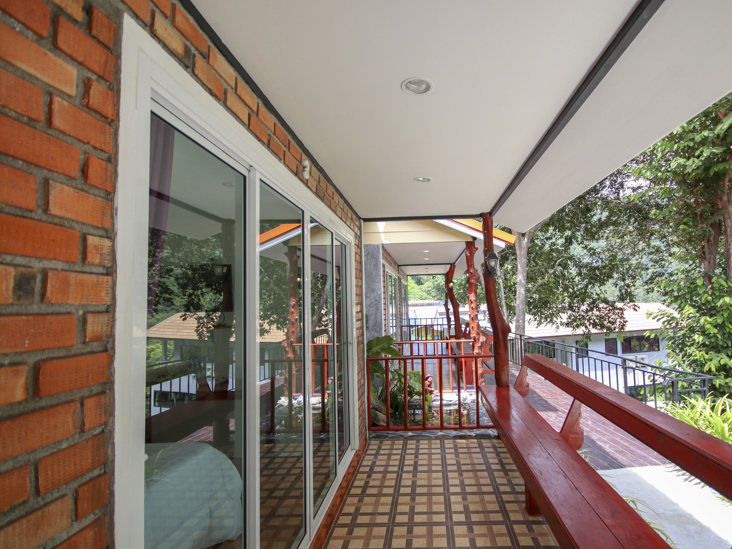 Varanda coberta com piso de azulejos, portas de correr de vidro e guarda-corpo vermelho.