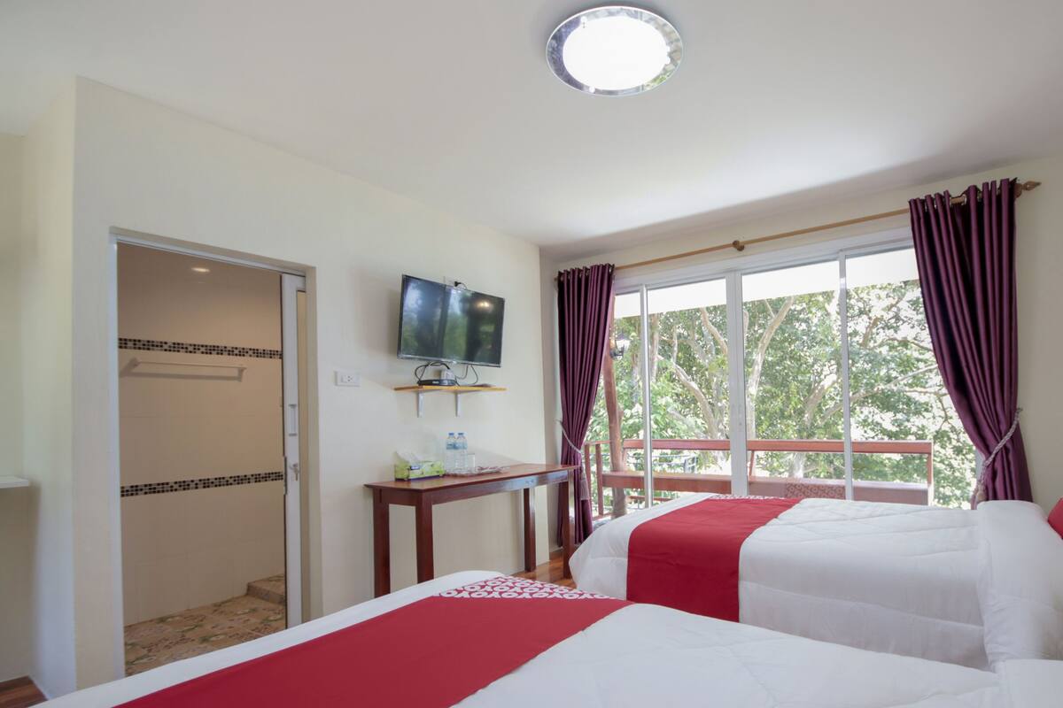 A hotel room with two beds, a TV mounted on the wall, a small table with a water bottle, and a window with curtains.