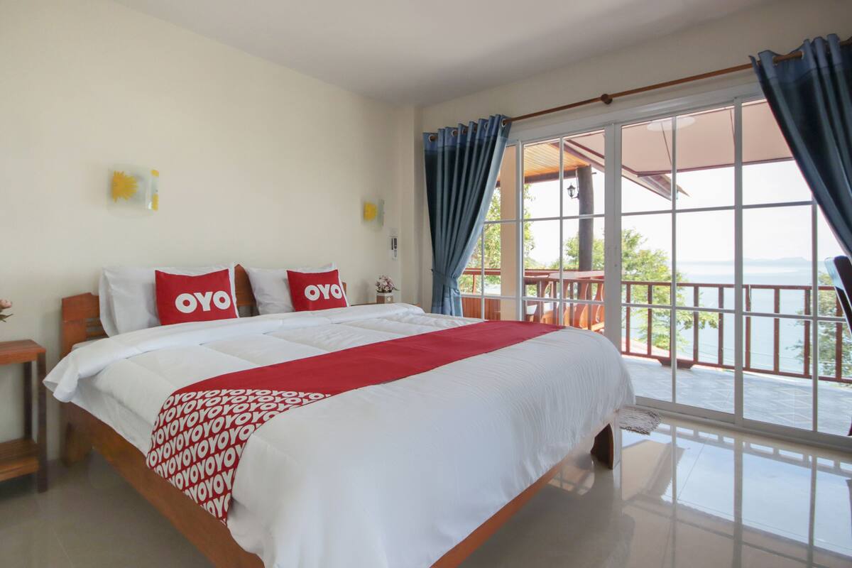 A bedroom with a large bed, a nightstand, a window with curtains, and a view of the outdoors.