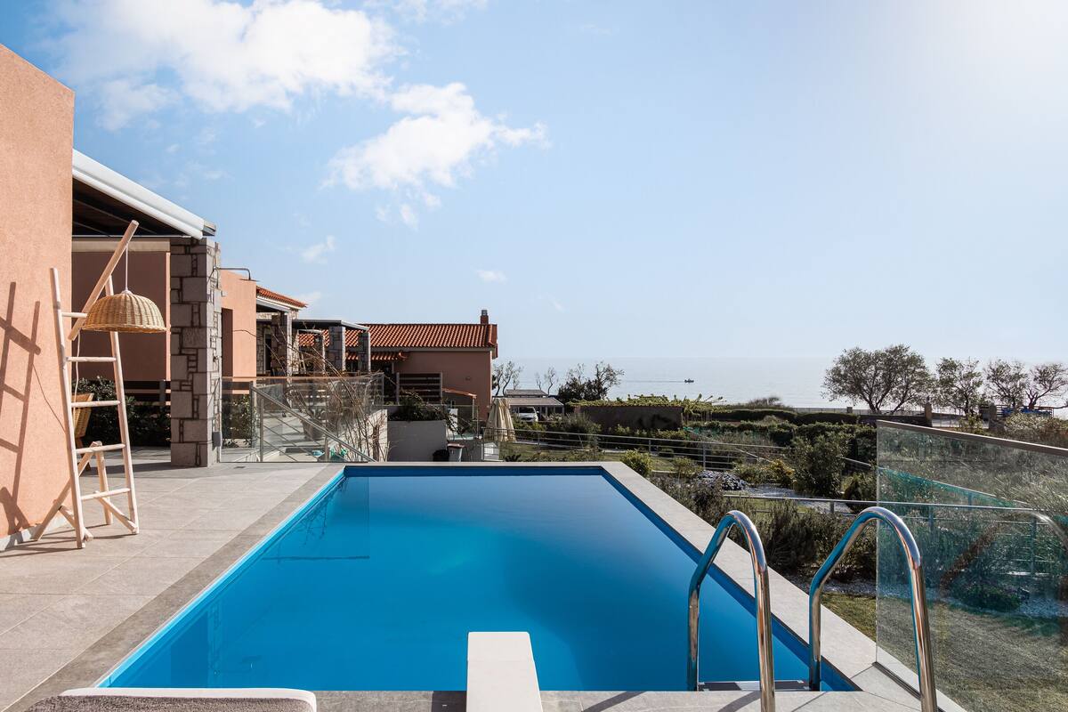 A swimming pool with a clear view of the sea, a wooden ladder, and a glass railing.