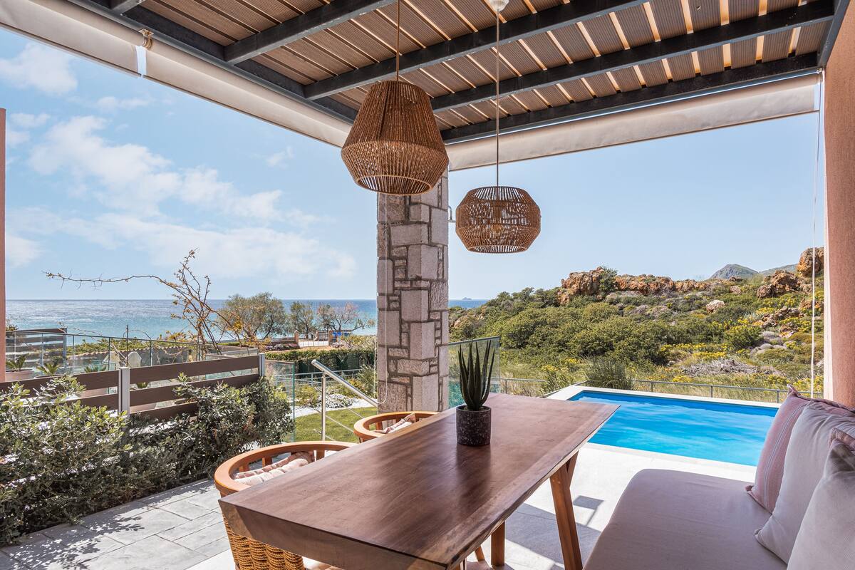 A terrace with a pool, stone pillar, wicker furniture, and a view of the sea and hills.