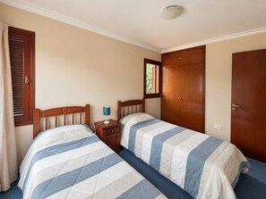 A bedroom with two beds, a wooden wardrobe, a nightstand with a lamp, and a window with blinds. - Family House for 6 People (Salta)
