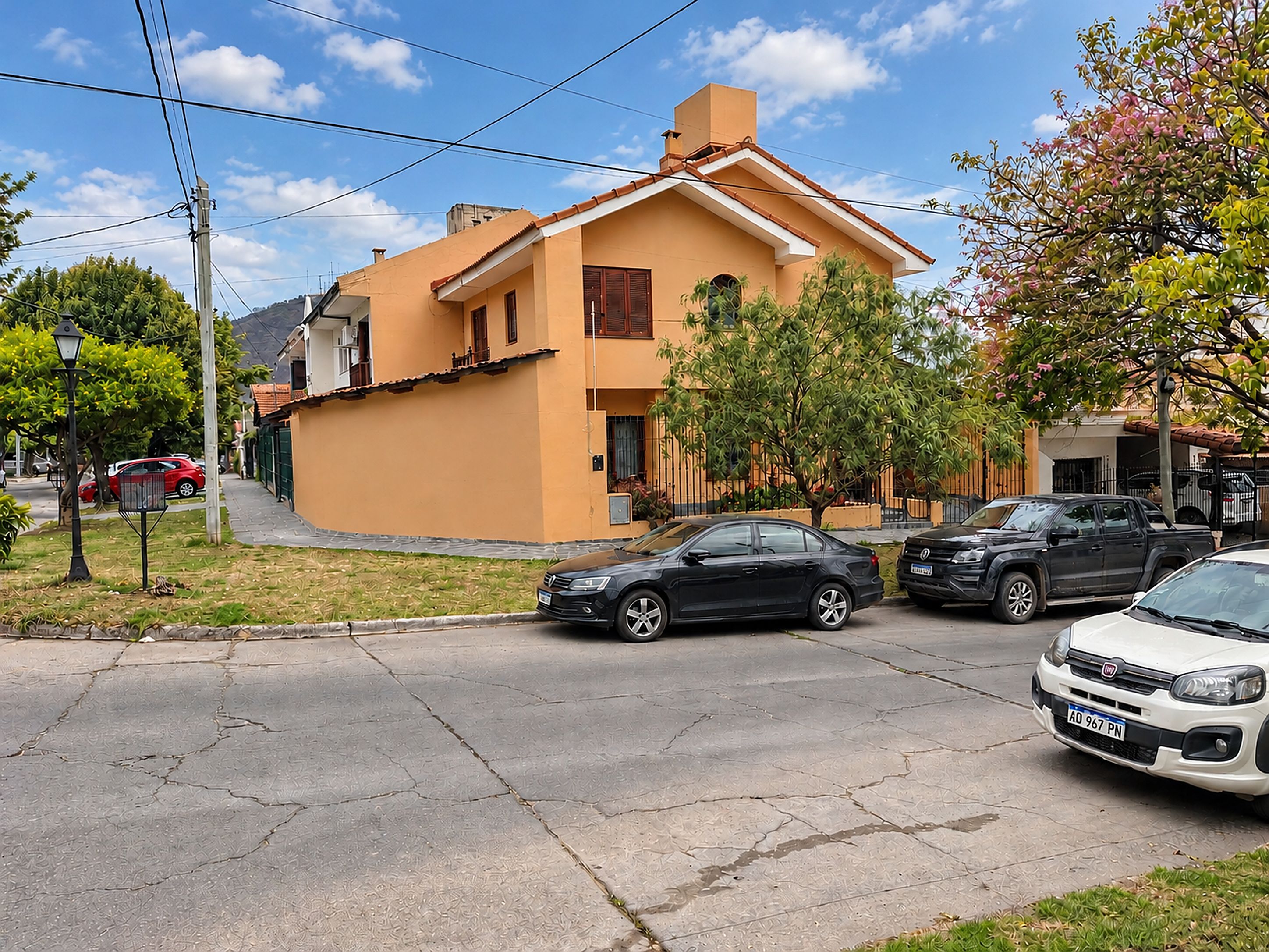 Een woonstraat met huizen, geparkeerde auto's en een heldere lucht.