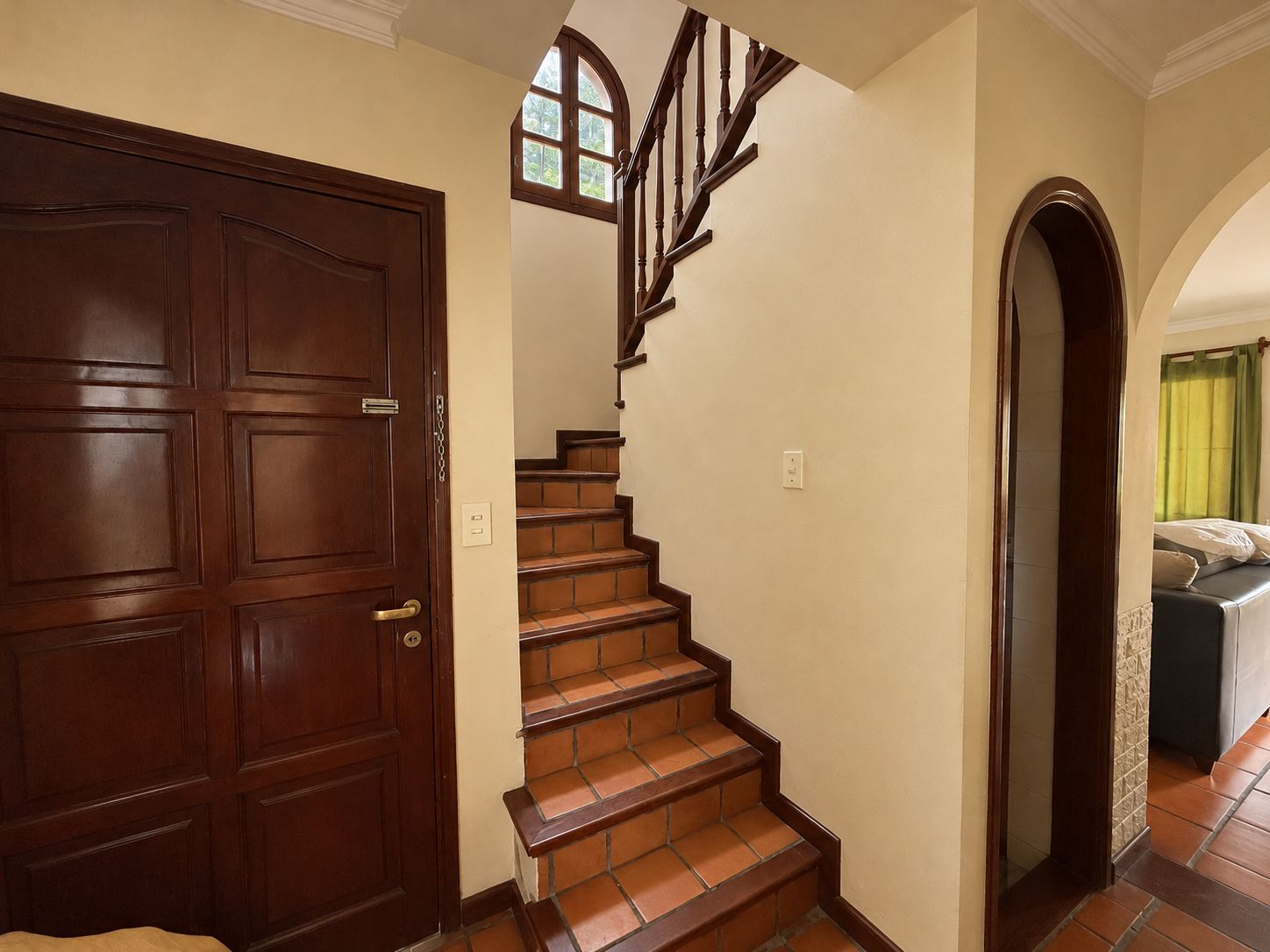 A wooden door with a brass handle, a staircase with brown steps and a wooden handrail, and a green curtain partially visible through an archway.