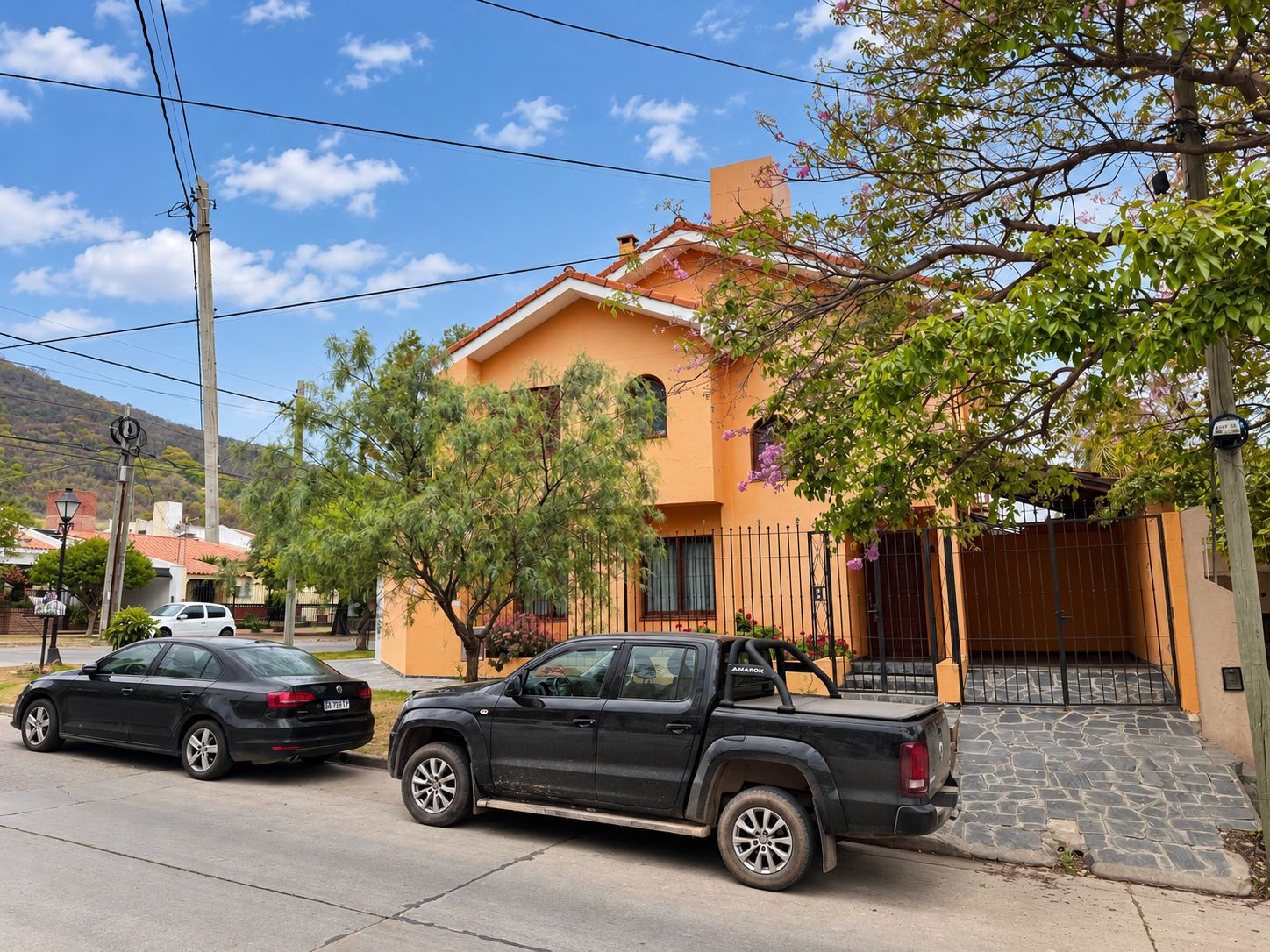Un barrio residencial con una casa de techo de tejas, un camino de entrada pavimentado y una camioneta negra estacionada.
