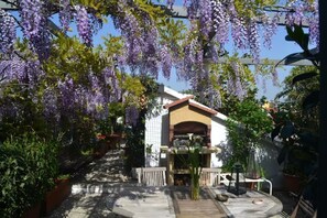 A covered outdoor area with hanging purple flowers, a tiled floor, and a small table with a lantern. - Apartment with terrace (Milano)