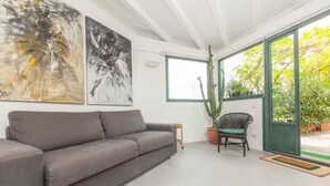 Un salon moderne avec un canapé gris, deux tableaux abstraits, un cactus et un fauteuil en osier.