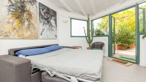 Une chambre moderne avec un lit, une chaise, un cactus et de grandes fenêtres.