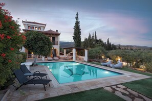 A pool area with lounge chairs, a pergola, and a view of the surrounding landscape. - Villa Nefeli (Ermionida)