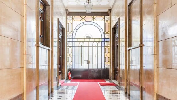 A hallway with a red carpet leading to a large arched doorway with intricate metalwork. - Dream House (Milano)