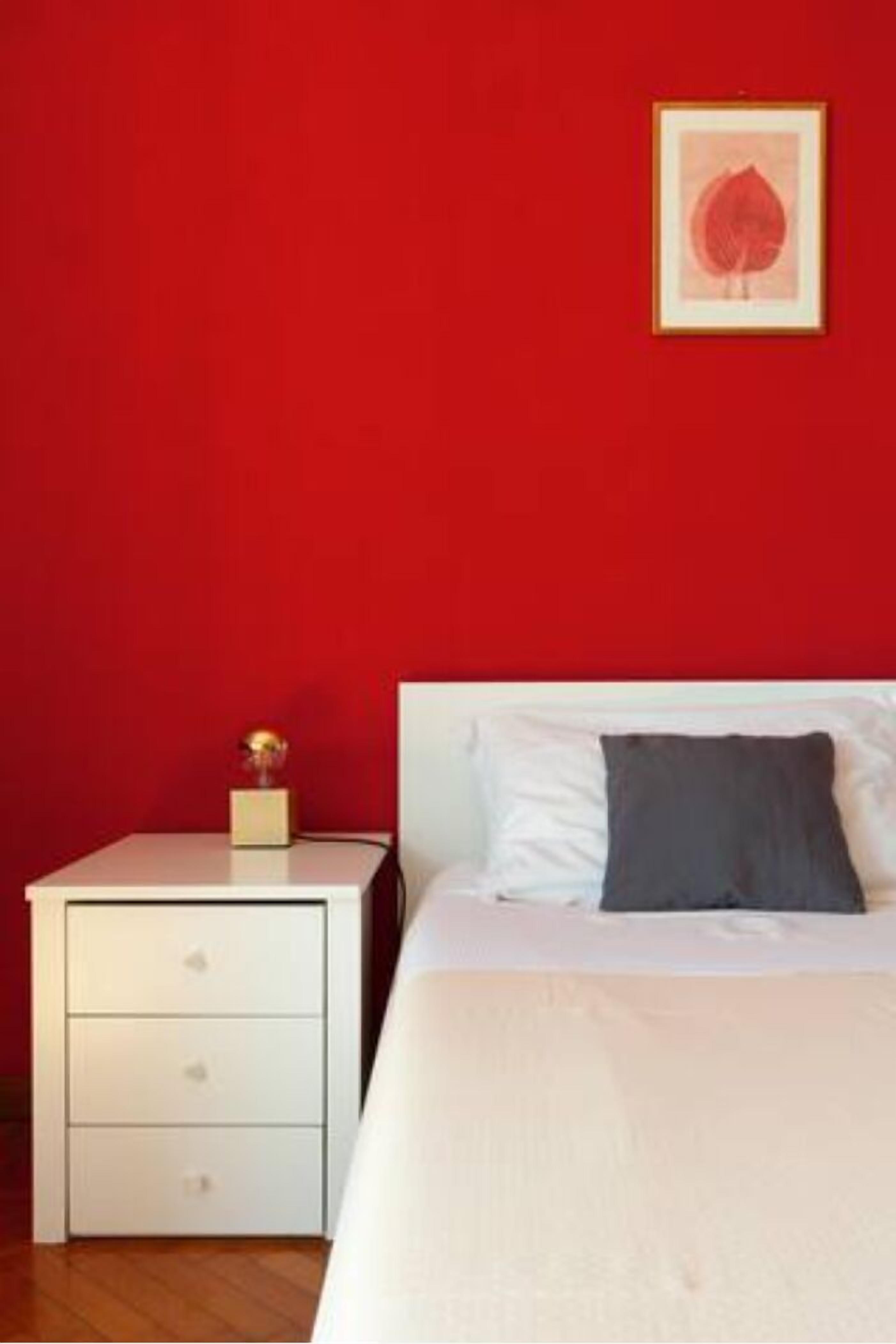 Une chambre avec un lit blanc, un oreiller gris, une table de chevet blanche avec des tiroirs et un tableau encadré accroché au mur.