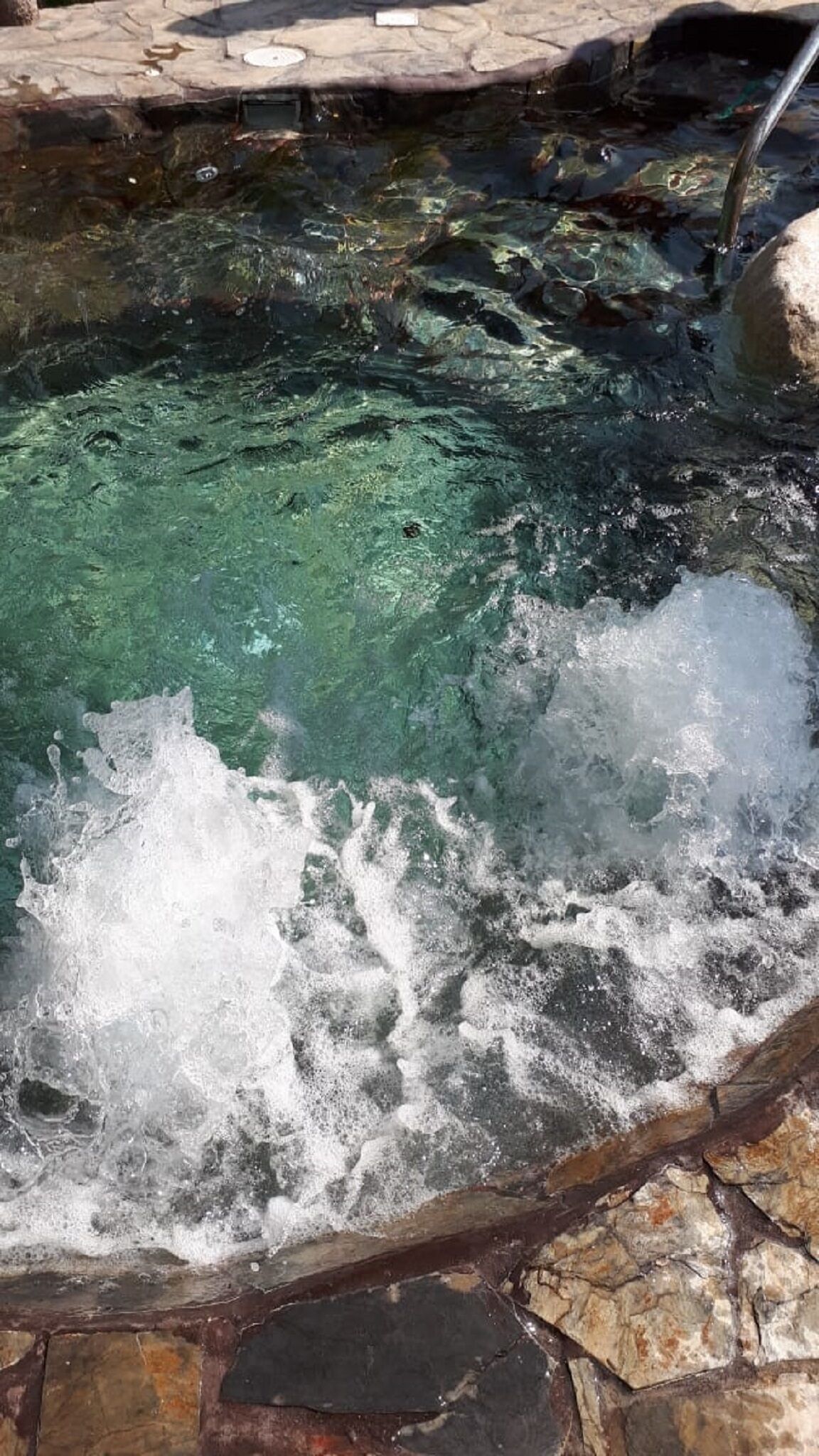 Une source thermale à l’eau claire et aux bulles visibles, entourée de dalles de pierre.