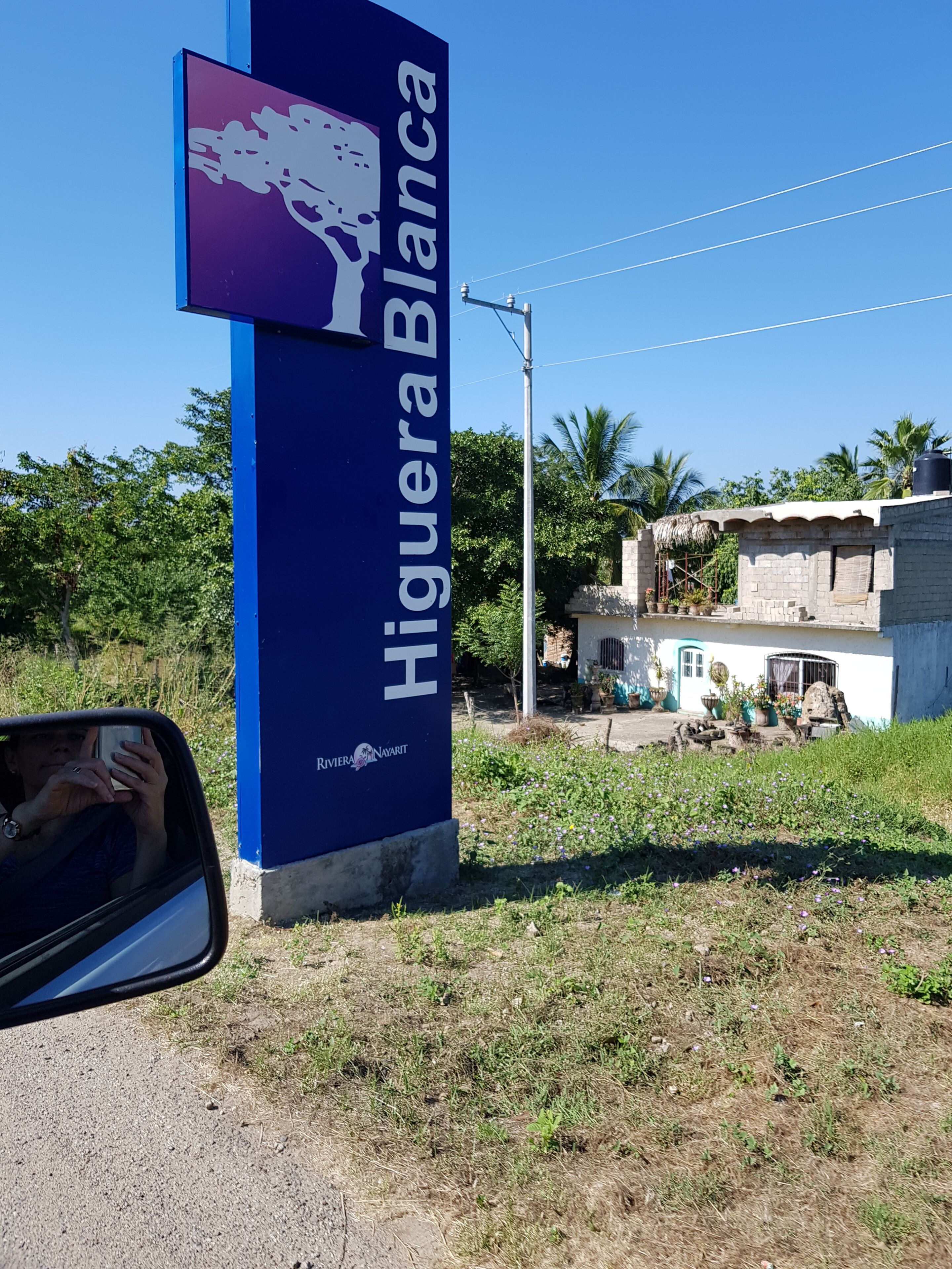A sign for 'Higuaera Blanca' with a logo, a streetlight, and a building in the background.