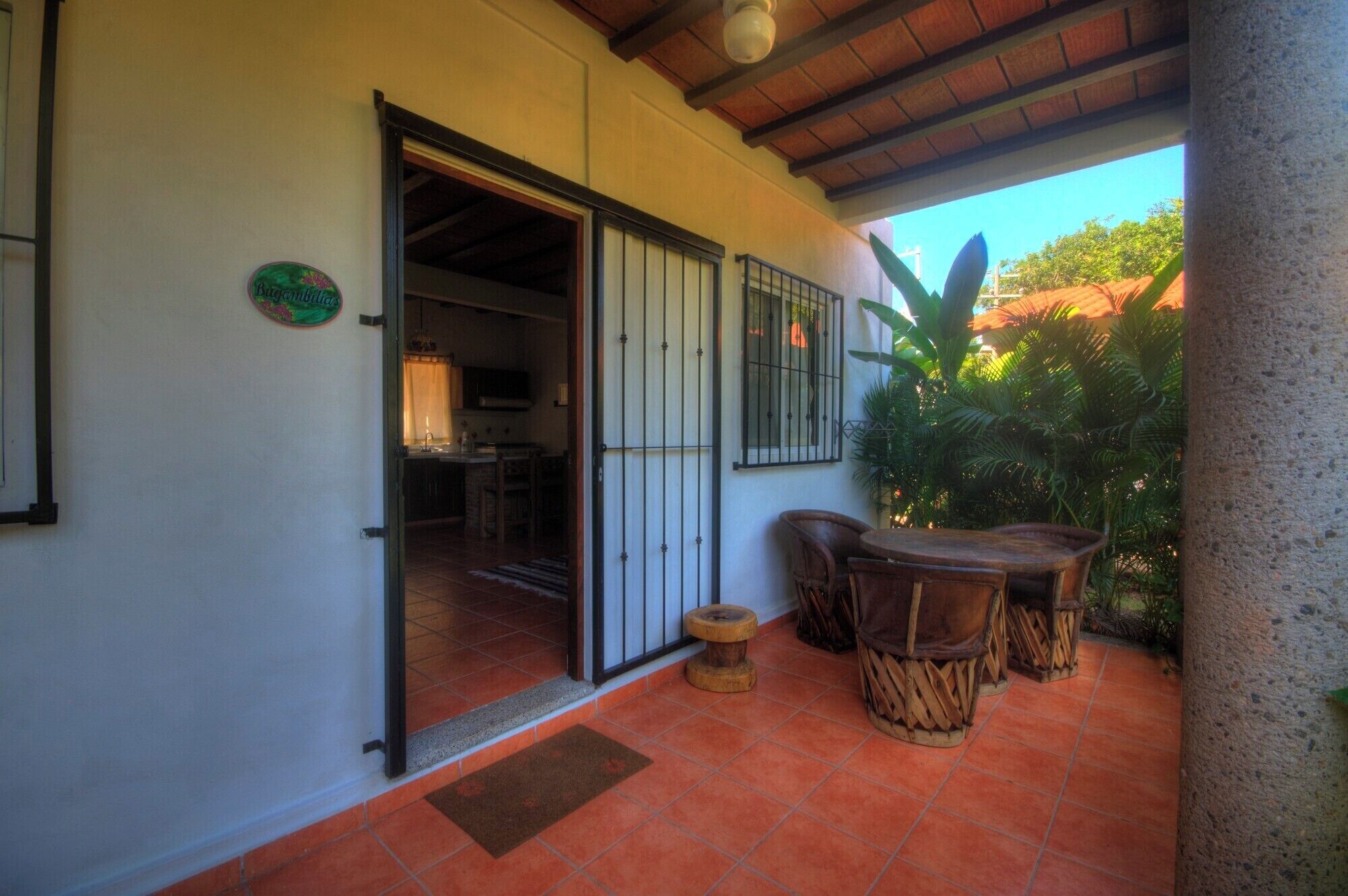 Un patio cubierto con una mesa y sillas de madera, piso de baldosas y una puerta que da a un espacio interior.