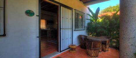 Un patio cubierto con una mesa y sillas de madera, piso de baldosas y una puerta que da a un espacio interior.