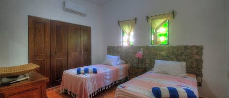 A bedroom with two beds, a wardrobe, a small table, and a ceiling fan.