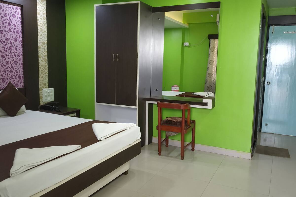 A hotel room with a bed, a desk with a chair, a wardrobe, and a door.