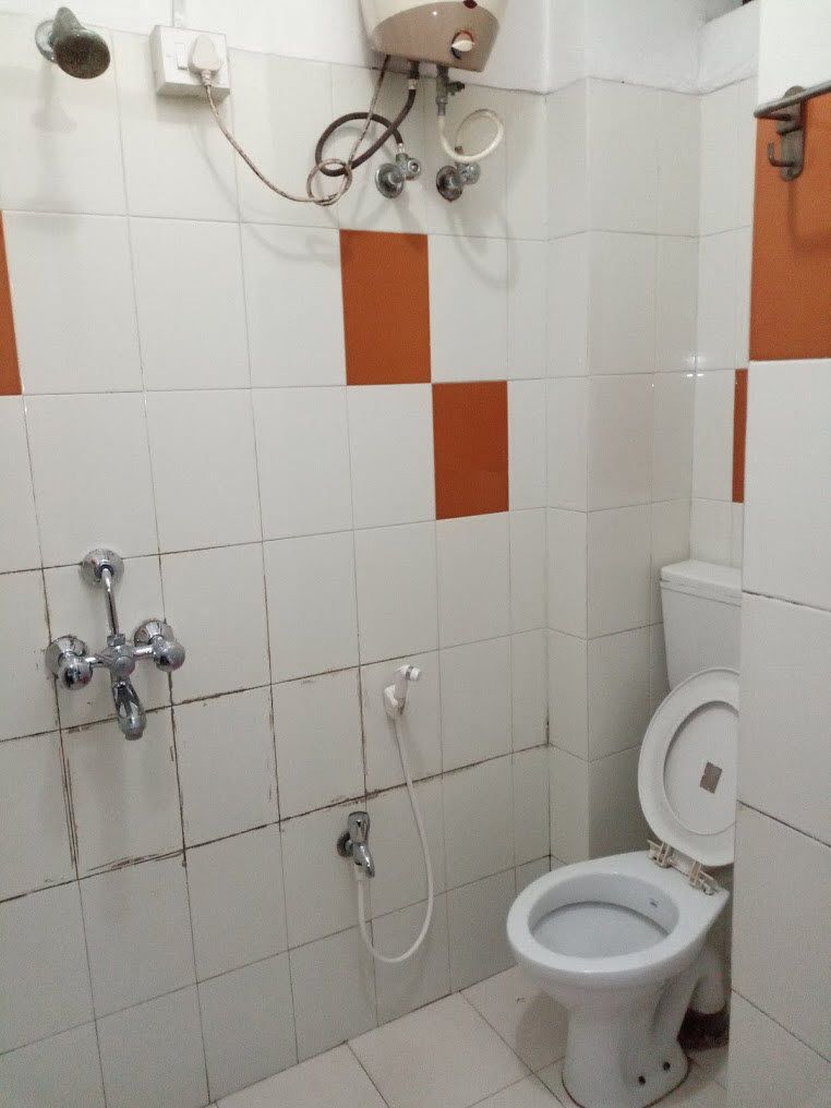A bathroom with white and orange tiles, a white toilet, and a shower with a handheld showerhead.