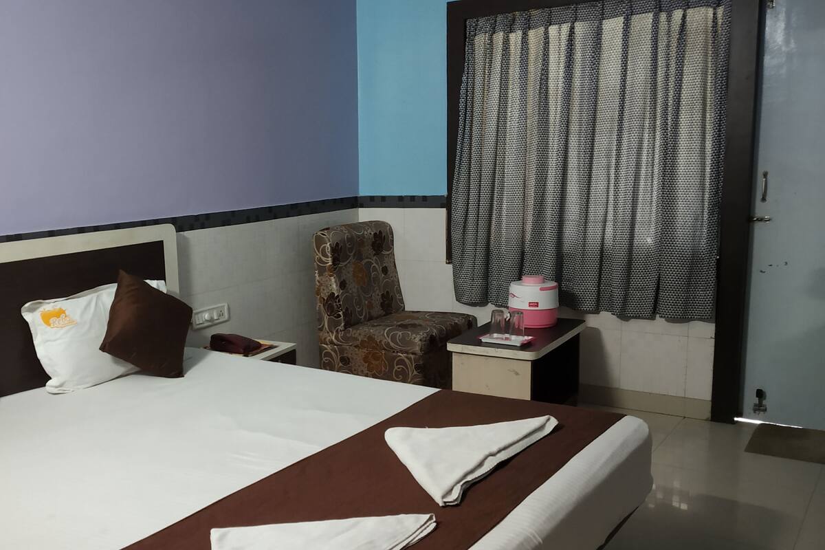 A hotel room with a bed, a chair, a small table, and a window with curtains.