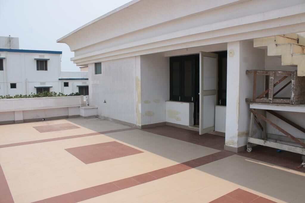 A rooftop terrace with a tiled floor, a white building with a black door, and a wooden structure on the right.