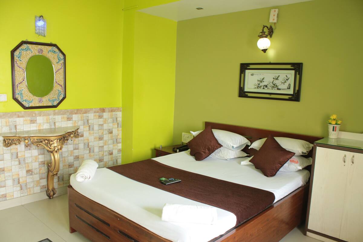 A hotel room with a bed, bedside table, and a mirror on the wall.