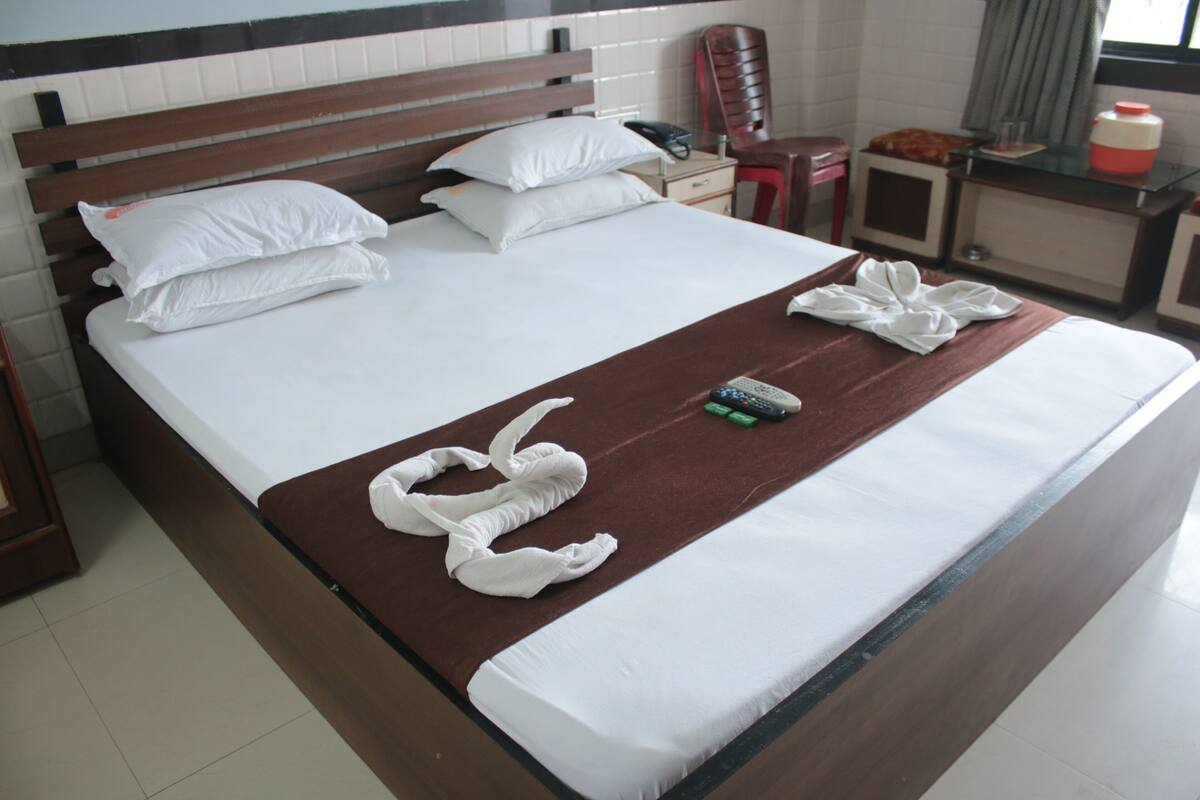 A neatly made bed with white linens, a brown bedspread, and two white towels folded on the bed.
