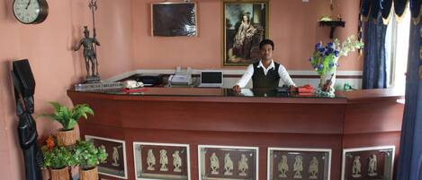 A reception desk with a receptionist, a clock, a framed portrait, and decorative items.
