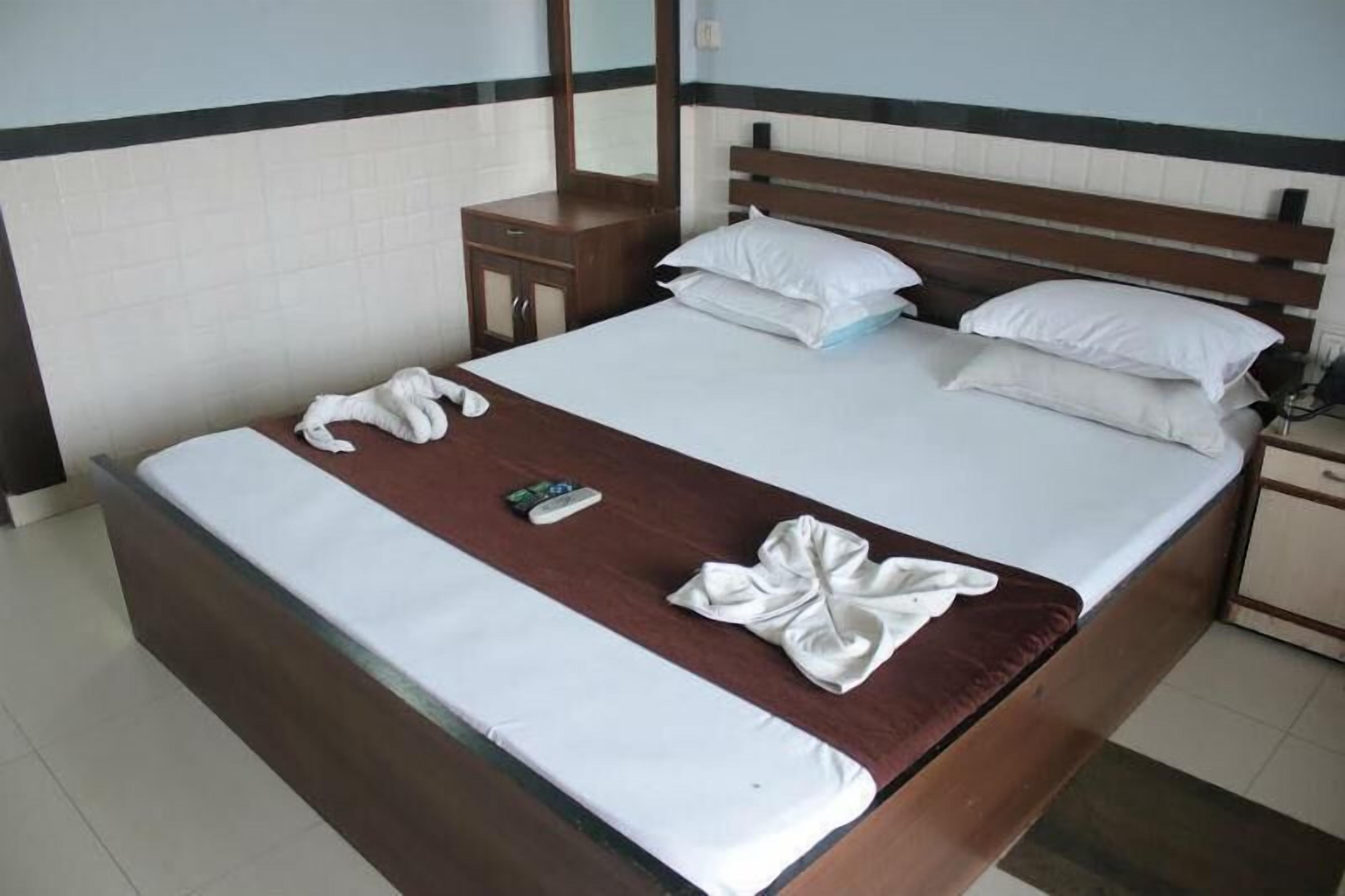 A neatly made bed with white linens, a brown headboard, and a wooden nightstand with a mirror.