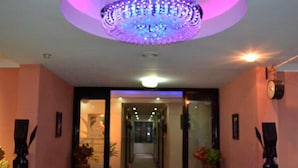 Un hall d’hôtel agrémenté d’un lustre, de plantes en pot et d’une horloge murale.