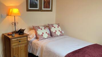 A neatly arranged bedroom with a bed, a bedside table with a lamp, a small cabinet, and two framed pictures on the wall.