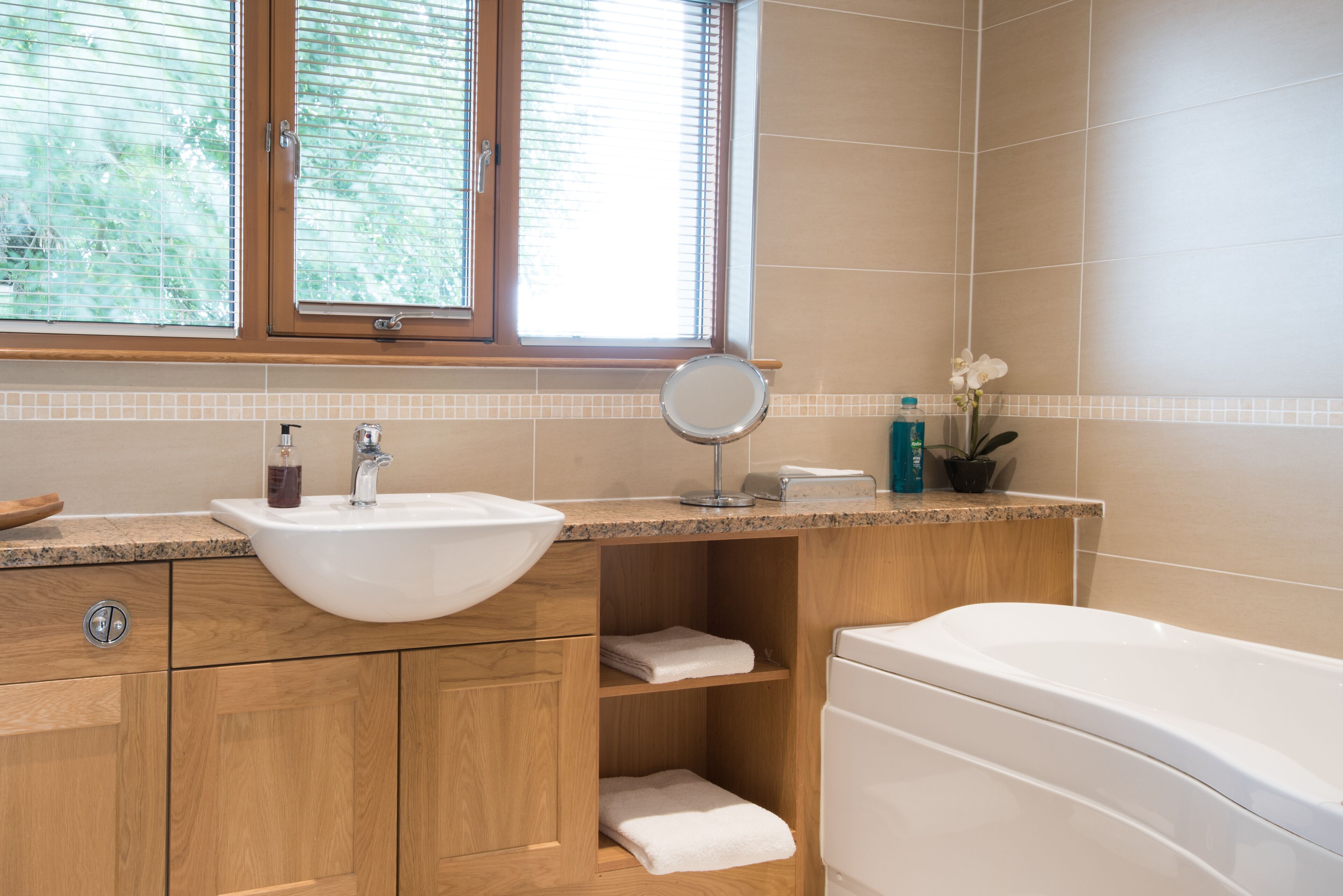 Un baño con tocador de madera, un lavabo blanco, un espejo, una bañera y una ventana con persianas.