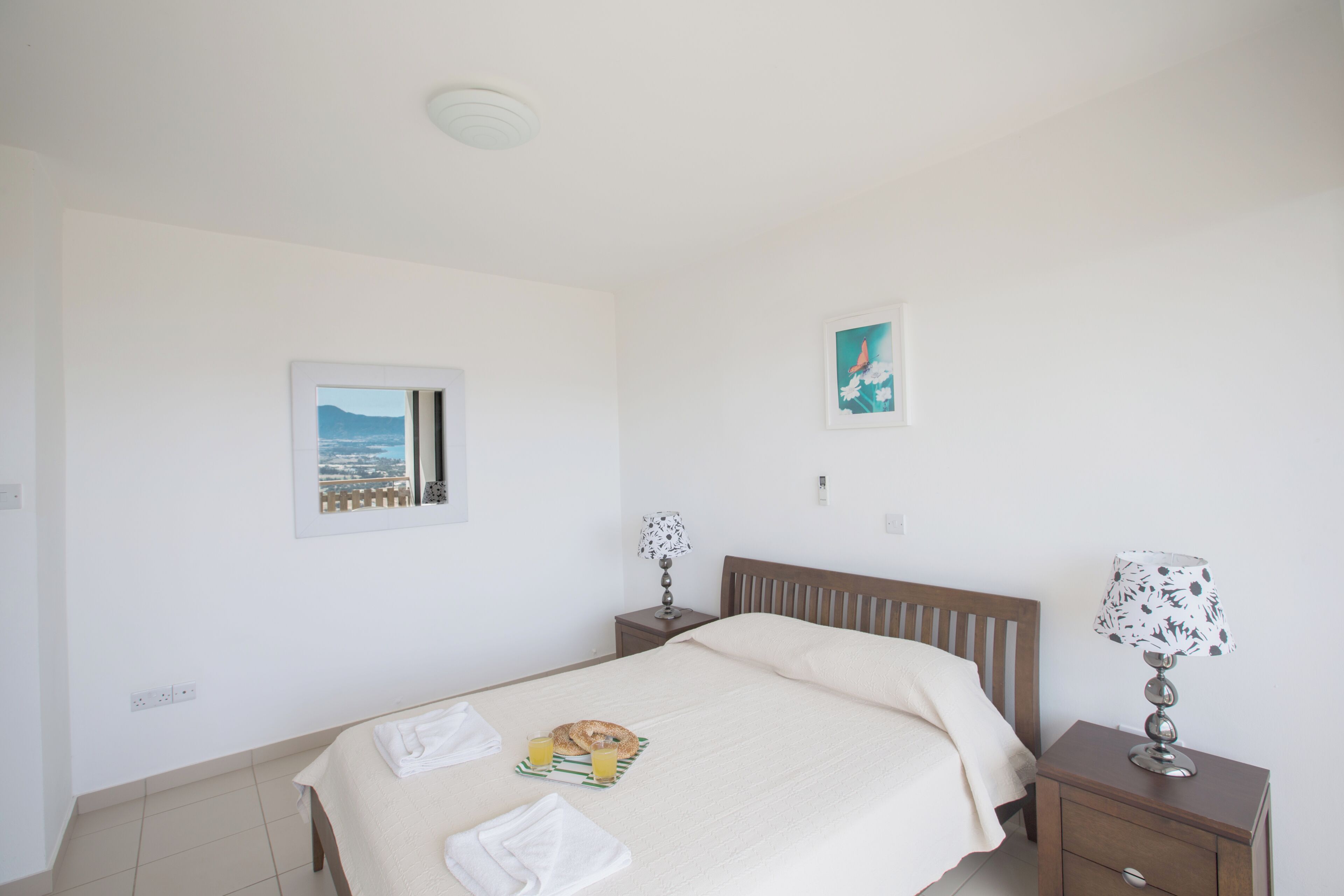 A bedroom with a bed, two bedside tables, a nightstand, a window with a view, and two wall-mounted pictures.