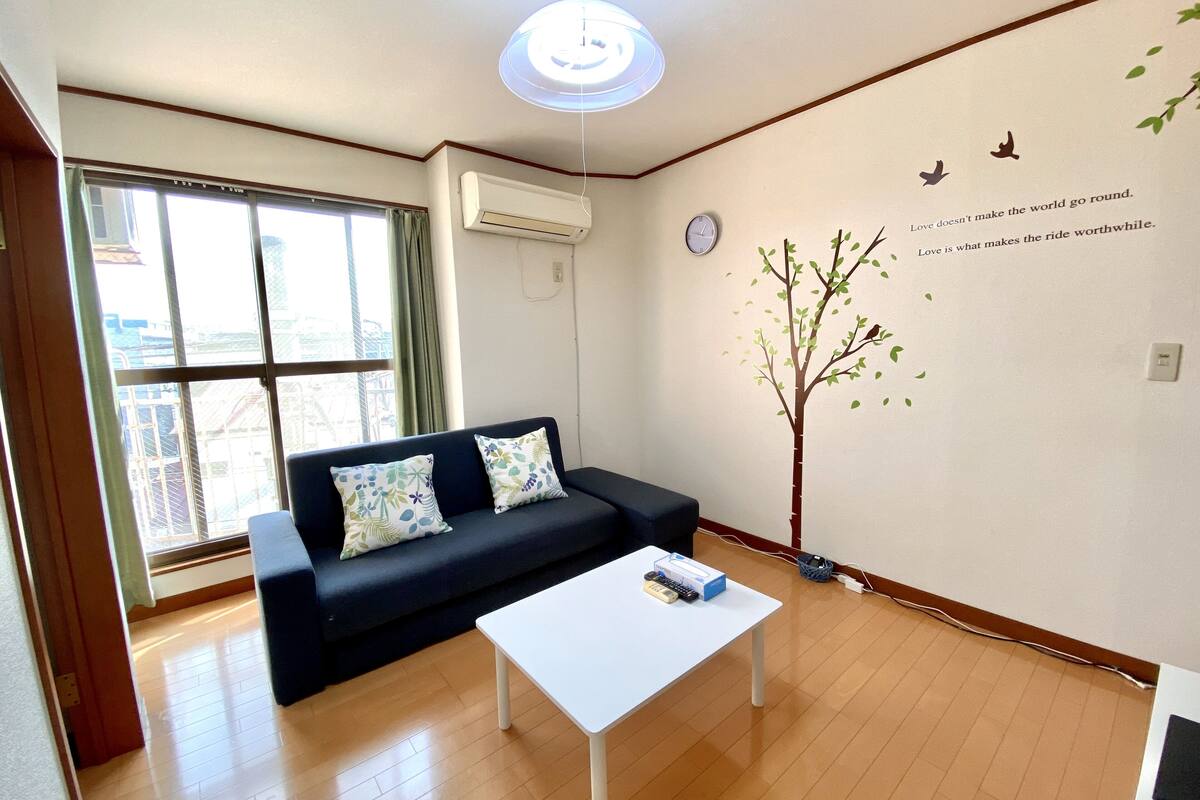 Una sala de estar con un sofá azul oscuro, una mesita de centro blanca y una pared decorada con un adhesivo de un árbol y citas inspiradoras.