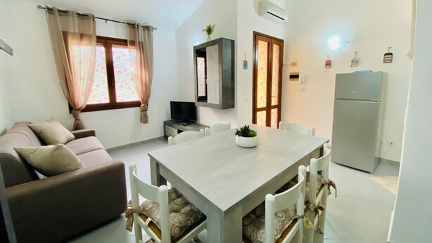 A compact living space with a sofa, dining table, chairs, a TV, and a refrigerator. - Appartamenti San Teodoro IV con BBQ, A/C e WIFI (San Teodoro)