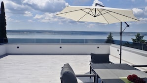 Une terrasse sur le toit avec vue sur la mer, une table avec un saladier de fruits et un parasol.