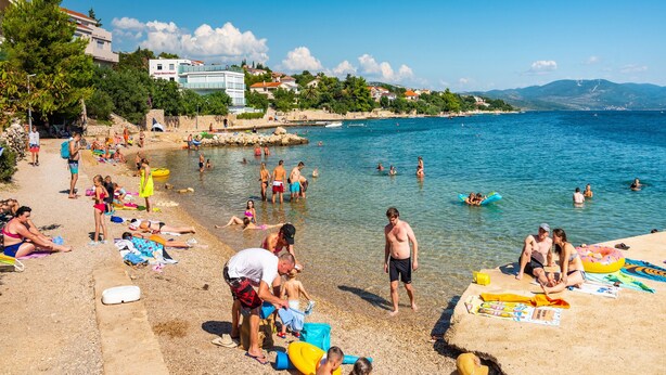 Une plage où l’on voit des gens nager et bronzer, un ciel dégagé et des bâtiments en arrière-plan.