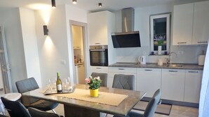 Une cuisine moderne avec des armoires blanches, une hotte de cuisinière en acier inoxydable et un téléviseur à écran plat fixé au-dessus du comptoir.