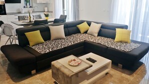 Un salon moderne avec un canapé d’angle, une table basse et un coin repas à l’arrière-plan.