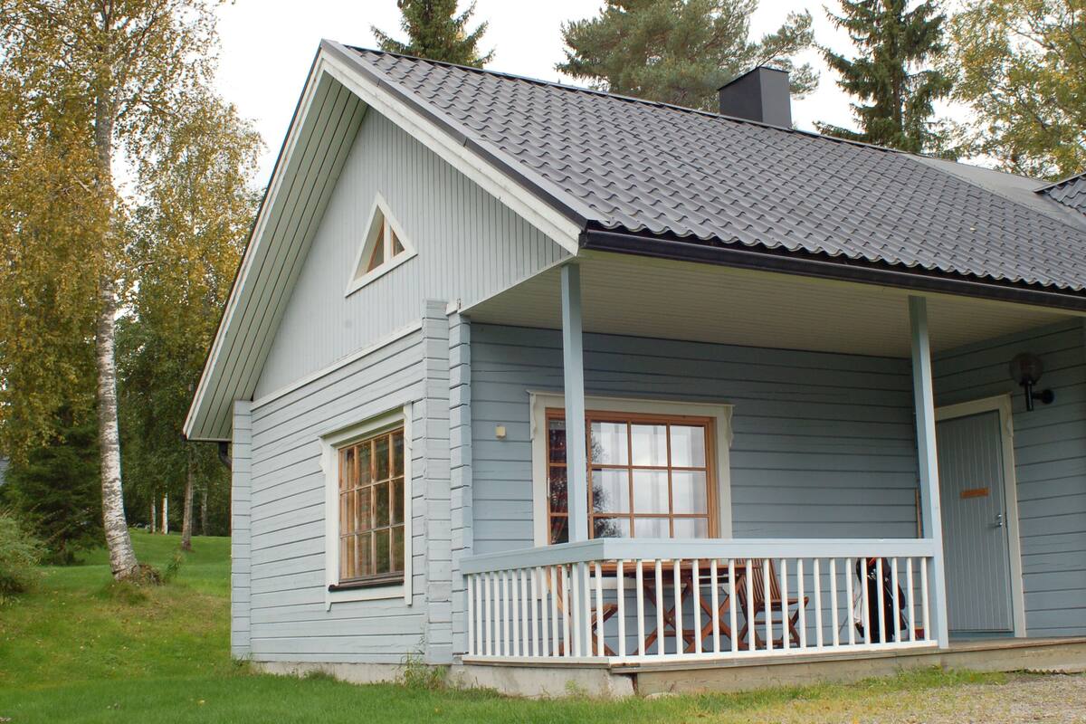 Ein hellblaues Holzhaus mit Veranda, großen Fenstern und Schornstein.