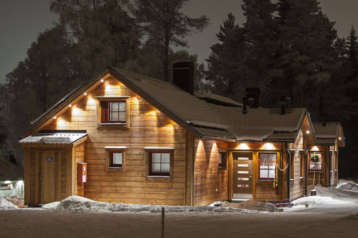 Eine Holzhütte mit geneigtem Dach, mehreren Fenstern und schneebedecktem Grund.