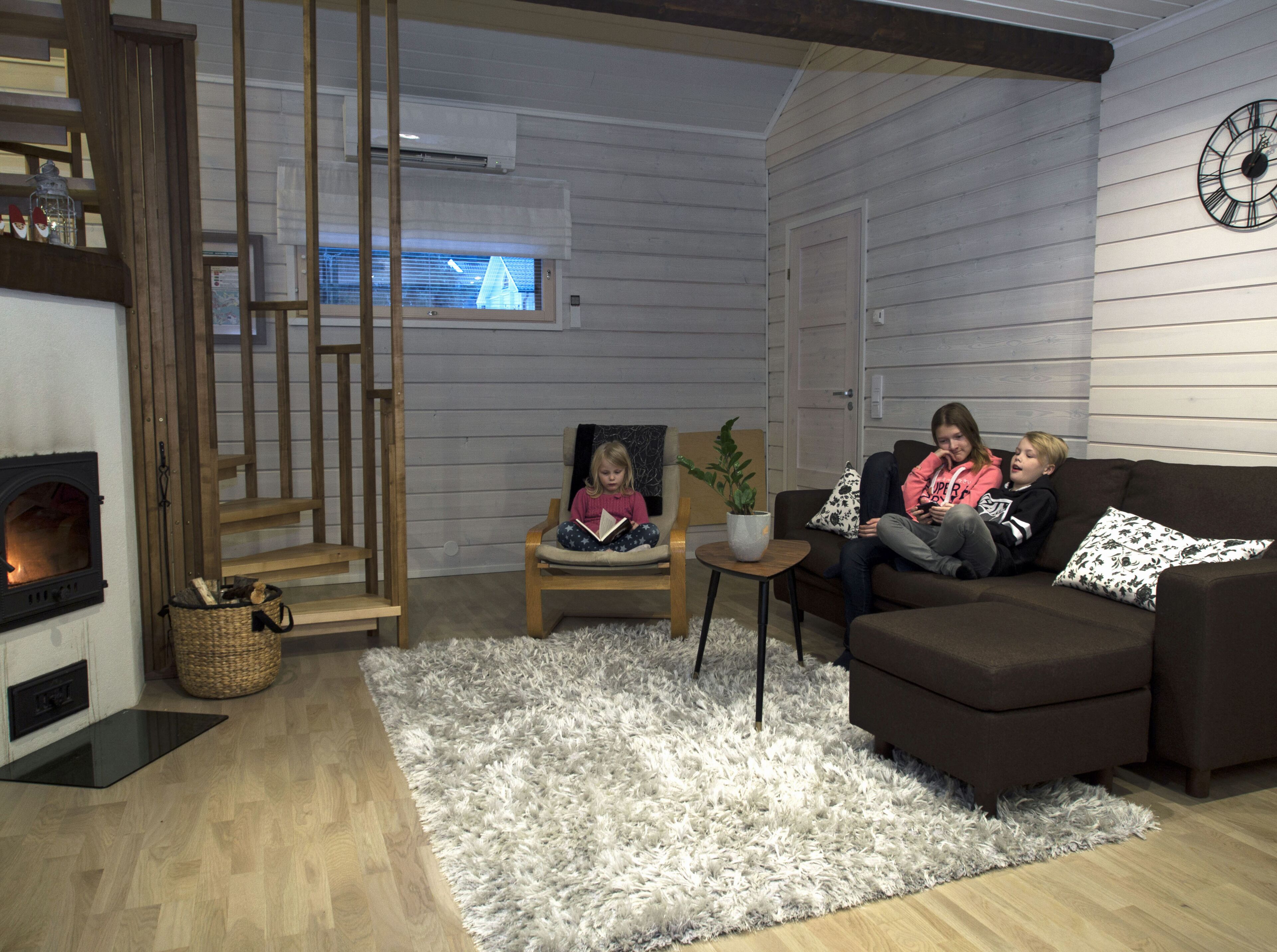 Een gezellige woonkamer met een open haard, een houten trap en een moderne klok aan de muur.