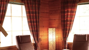 L’intérieur d’une cabane en rondins, avec deux fauteuils en cuir marron, un tapis bleu et des rideaux à carreaux sur les murs et les fenêtres en bois.
