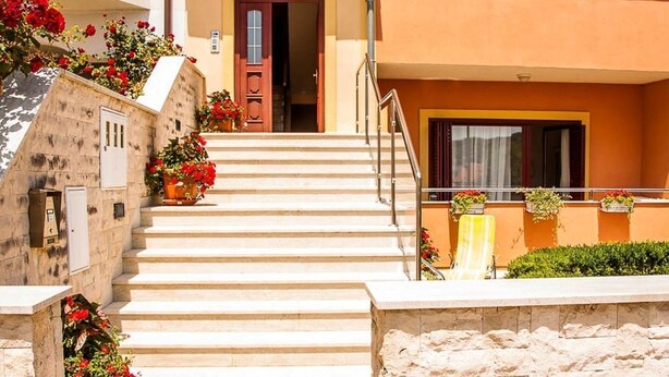 A building with a stone facade, a set of stairs leading to a door, and potted plants with red flowers. - Apartments "Labinac" Pula- Apartment I (Pula)
