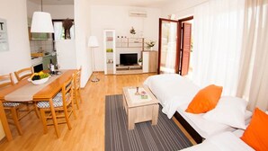 A modern living room with a sofa, dining table, and chairs. There is a TV and a small kitchen area in the background. - Apartments "Labinac" Pula- Apartment I (Pula)